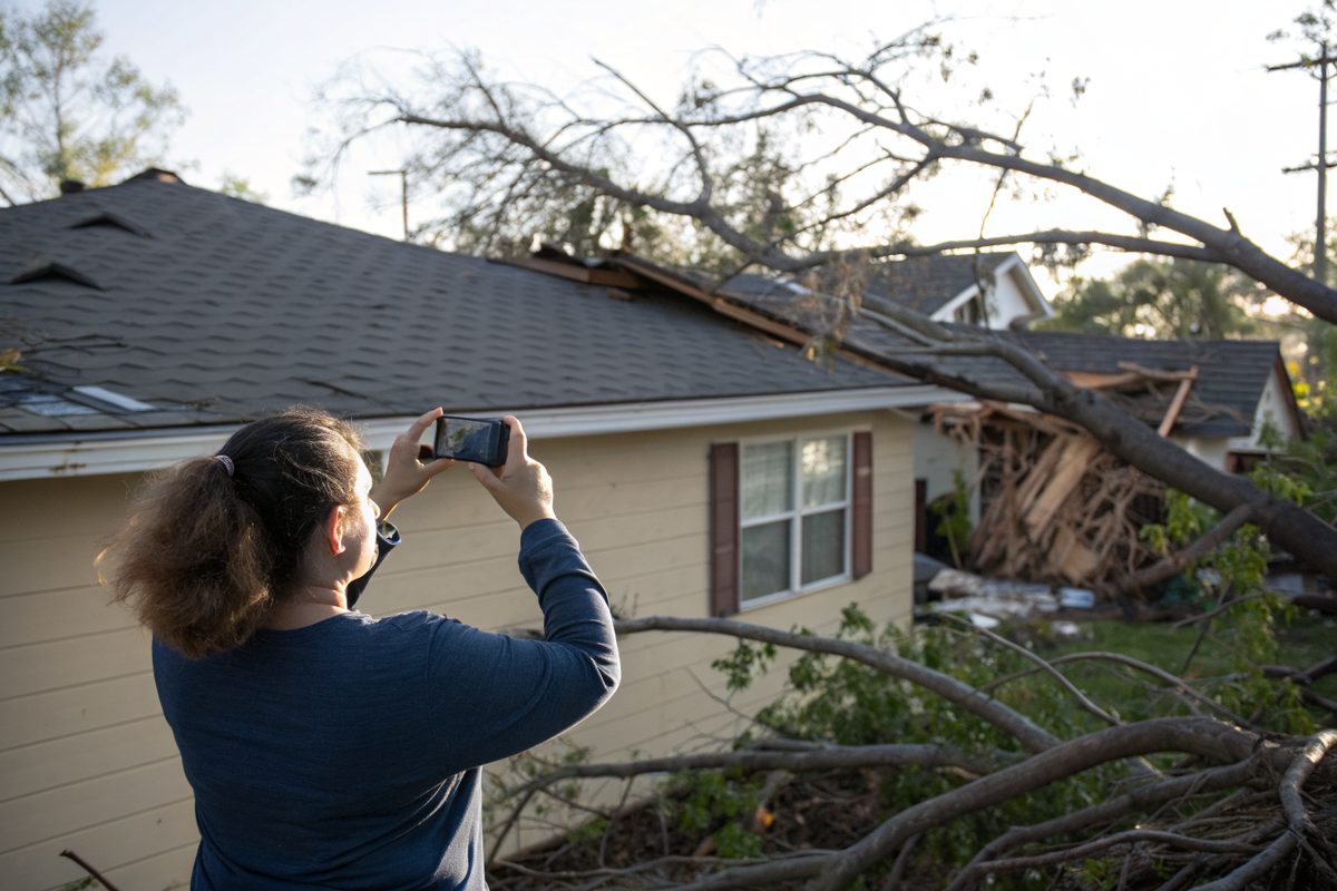 A homeowner photographing her roof with a phone after a windstorm